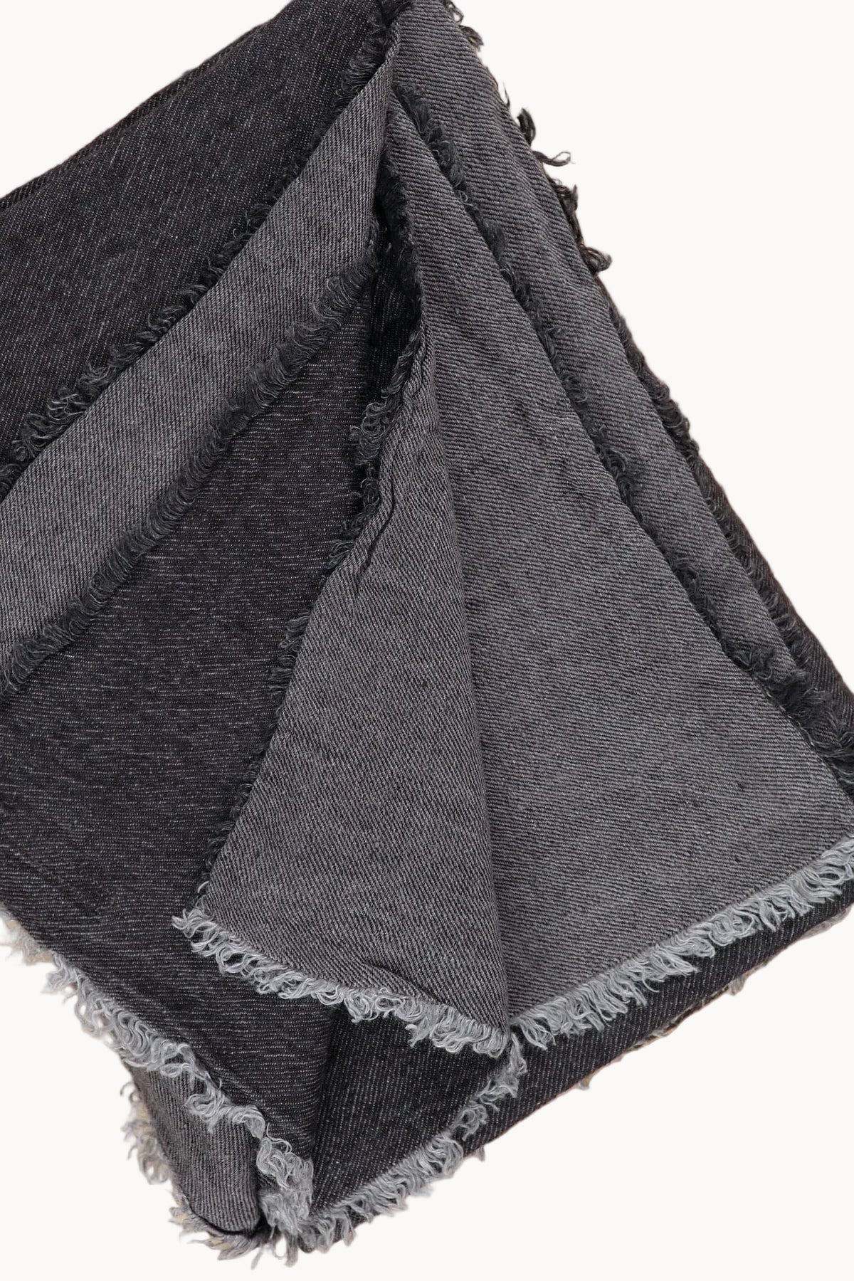 A folded dark gray woven blanket with frayed edges, laid on a light wood surface.
