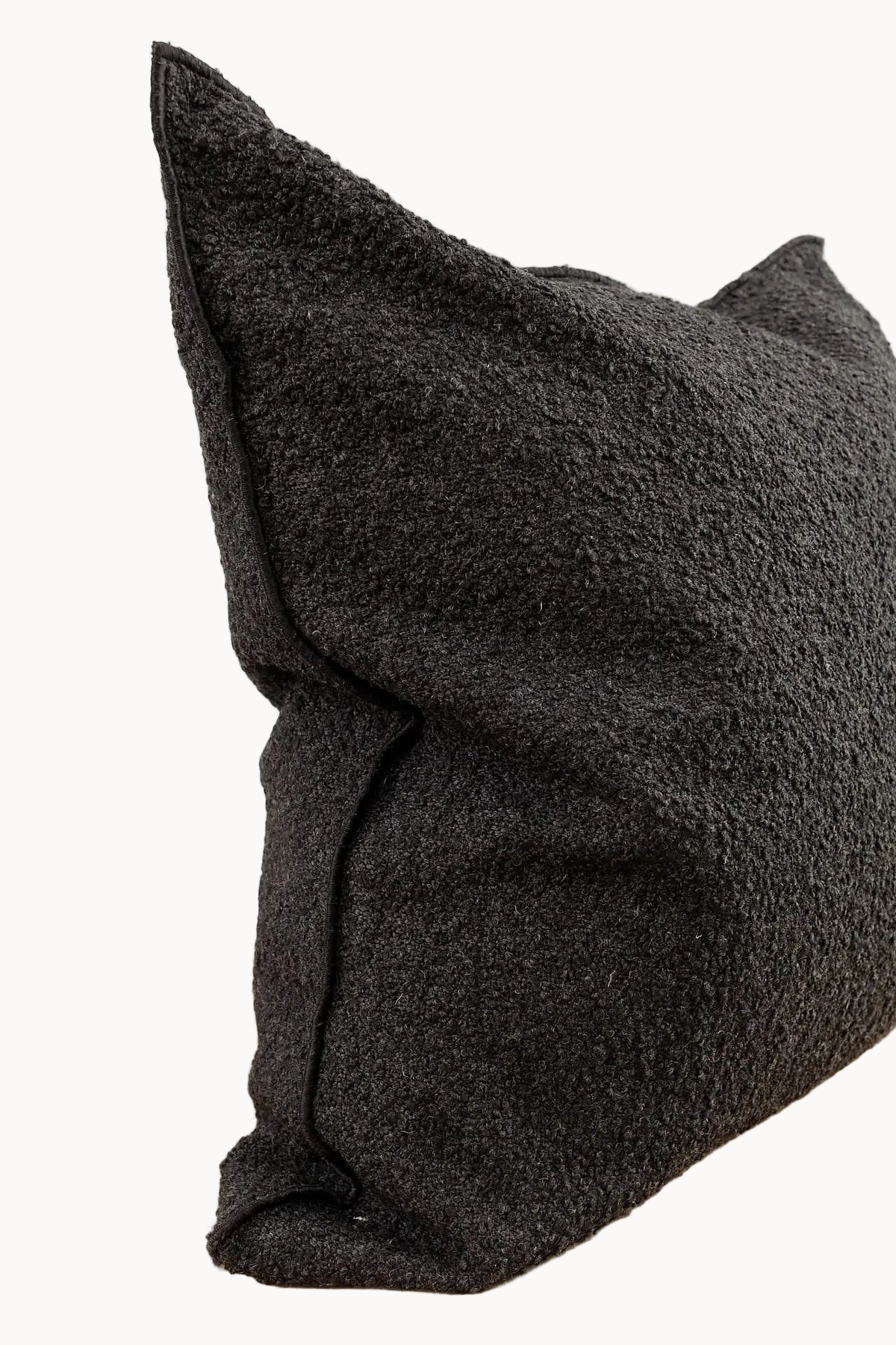 A close-up of a textured black throw pillow with a bouclé-like fabric against a plain off-white background.